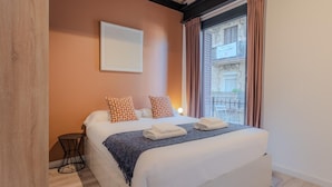 A bedroom with a bed, pillows, a blanket, a bedside table, and a window with curtains. - Sants Montjuic Olympic View (Barcelona)