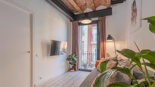 A modern living room with a sofa, a TV mounted on the wall, a potted plant, and a view of the outside balcony. - Sants Montjuic Olympic View (Barcelona)