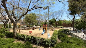 A playground with swings, slides, and climbing structures surrounded by trees and greenery. - Sants Montjuic Olympic View (Barcelona)