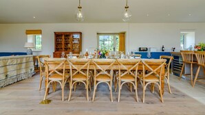 Un vaste espace dédié à la salle à manger, avec une table et des chaises en bois, un meuble à vin et une vue sur l’extérieur grâce à de grandes fenêtres.
