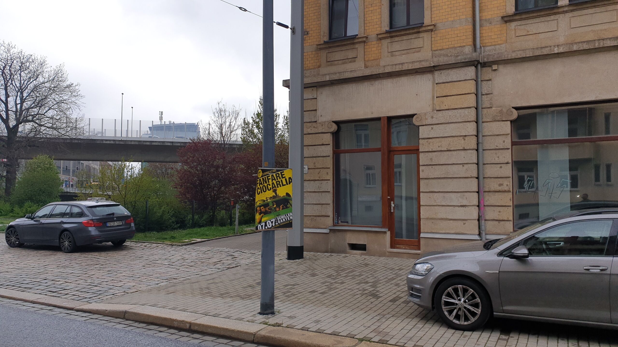 A building with a brick facade and large windows, a parked car, and a sign on a pole.