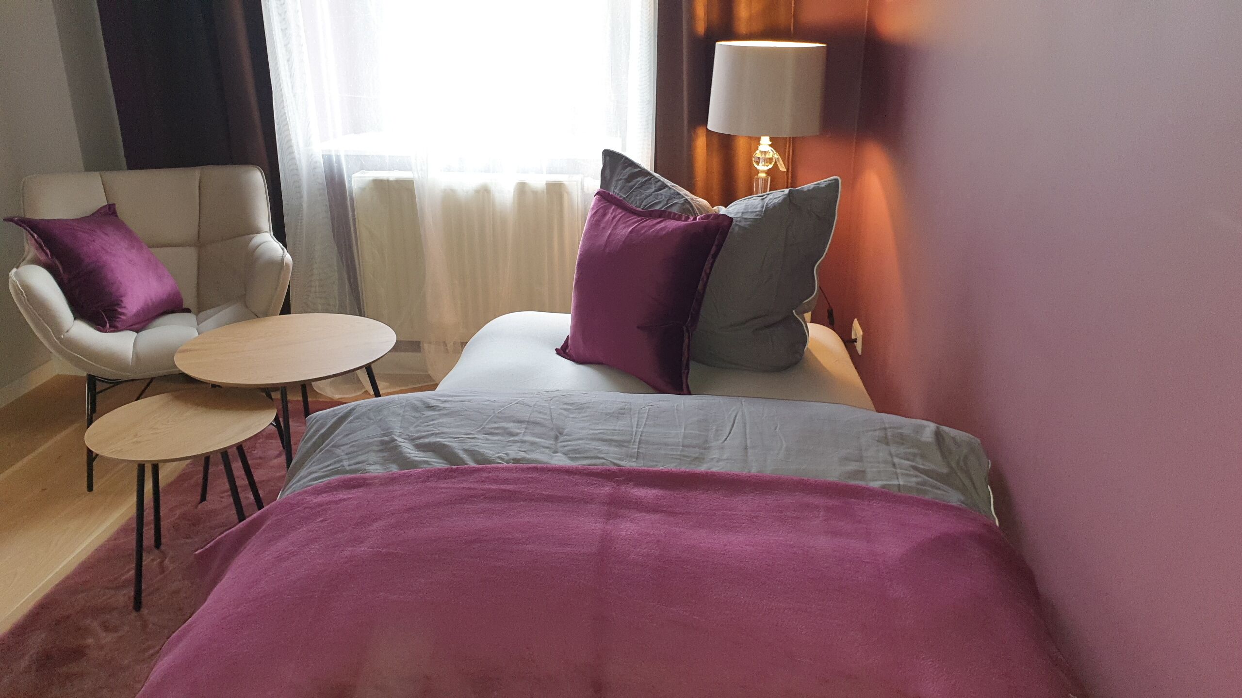 A hotel room with a bed, two chairs, a small table, and a lamp.