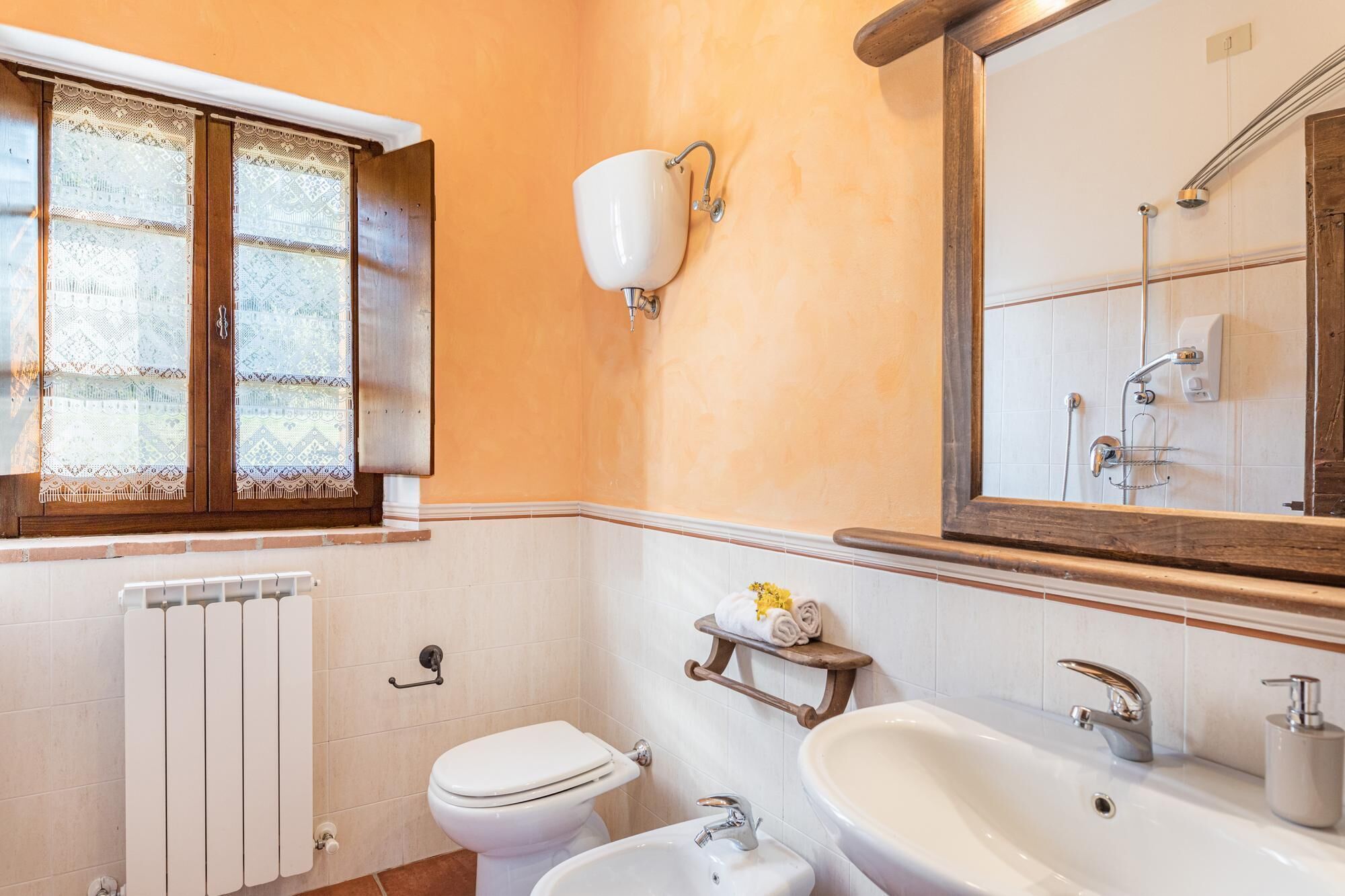 Casa de banho com sanita, bidé, lavatório e janela com cortinas de renda.