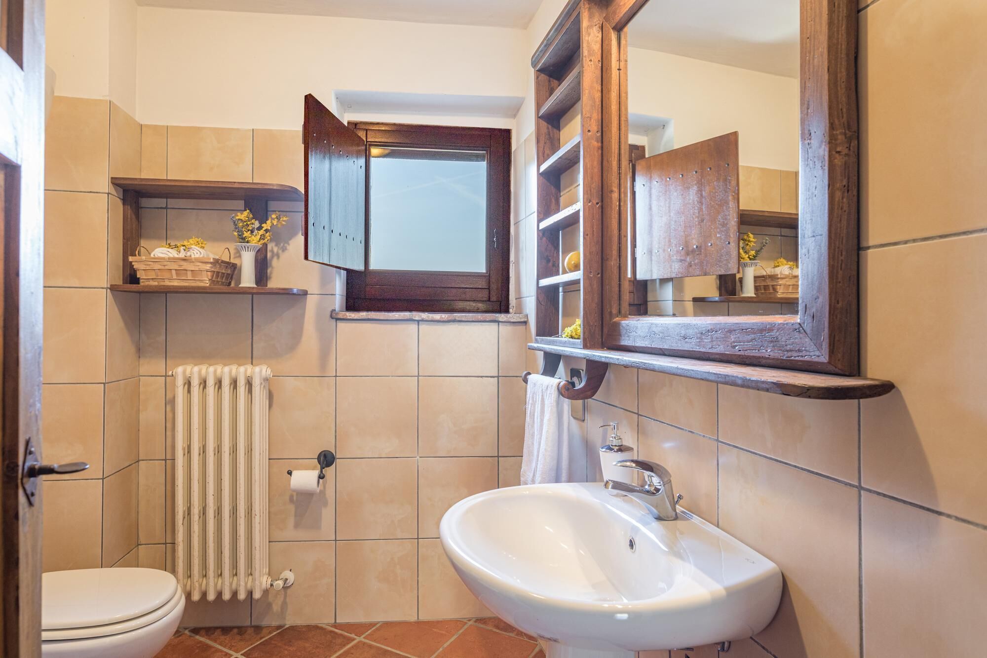 Un baño con inodoro, lavamanos blanco, espejo y toallero.