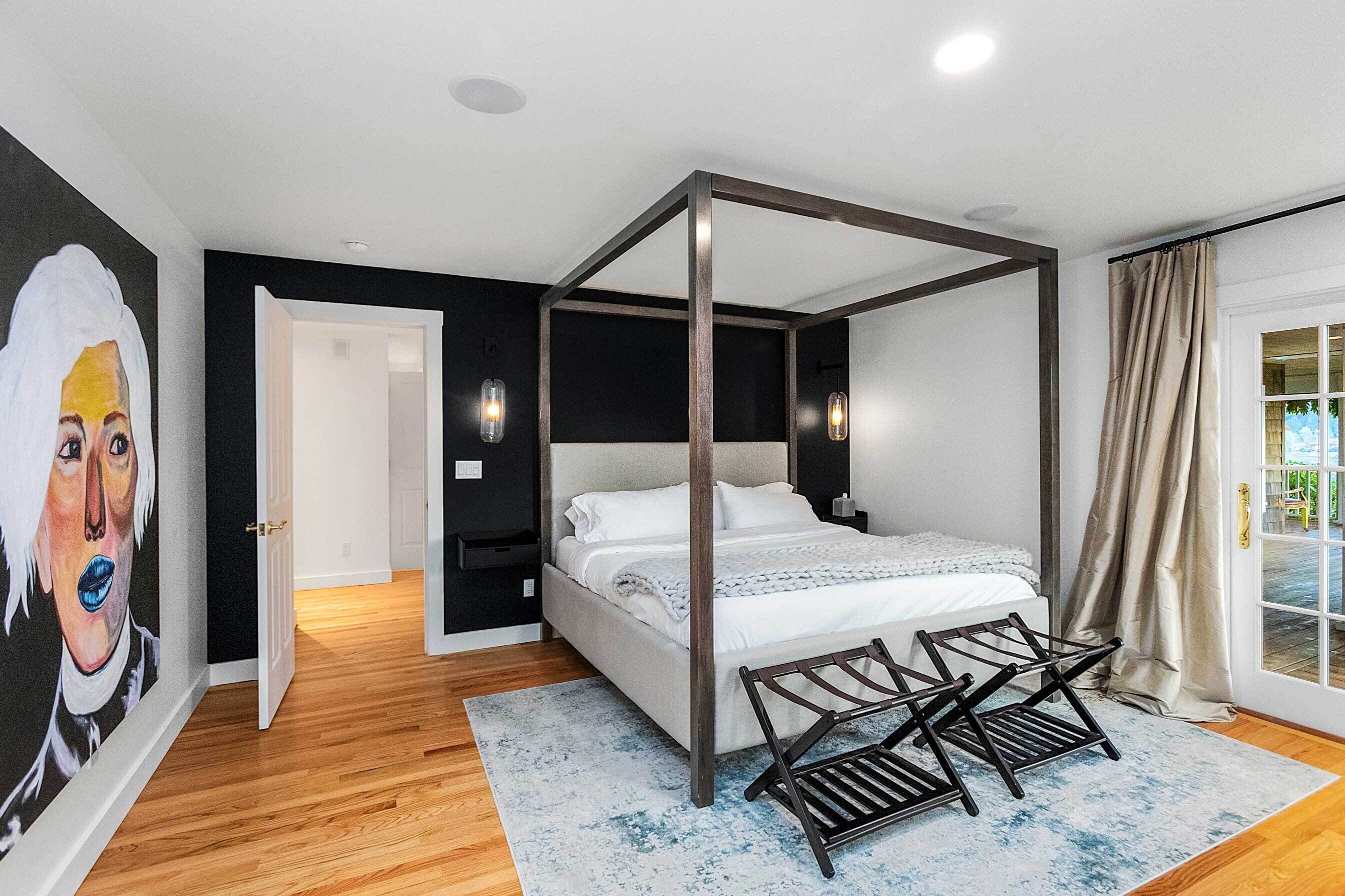 Un dormitorio con cama con dosel, piso de madera, un ventanal con cortinas y un cuadro en la pared.