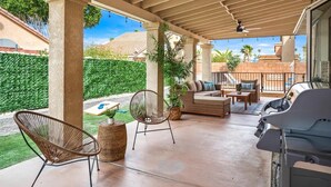 A covered patio with a grill, wicker chairs, a sofa, and a ceiling fan.