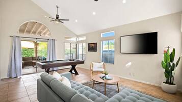 A spacious living room with a pool table, comfortable seating, and a large TV.
