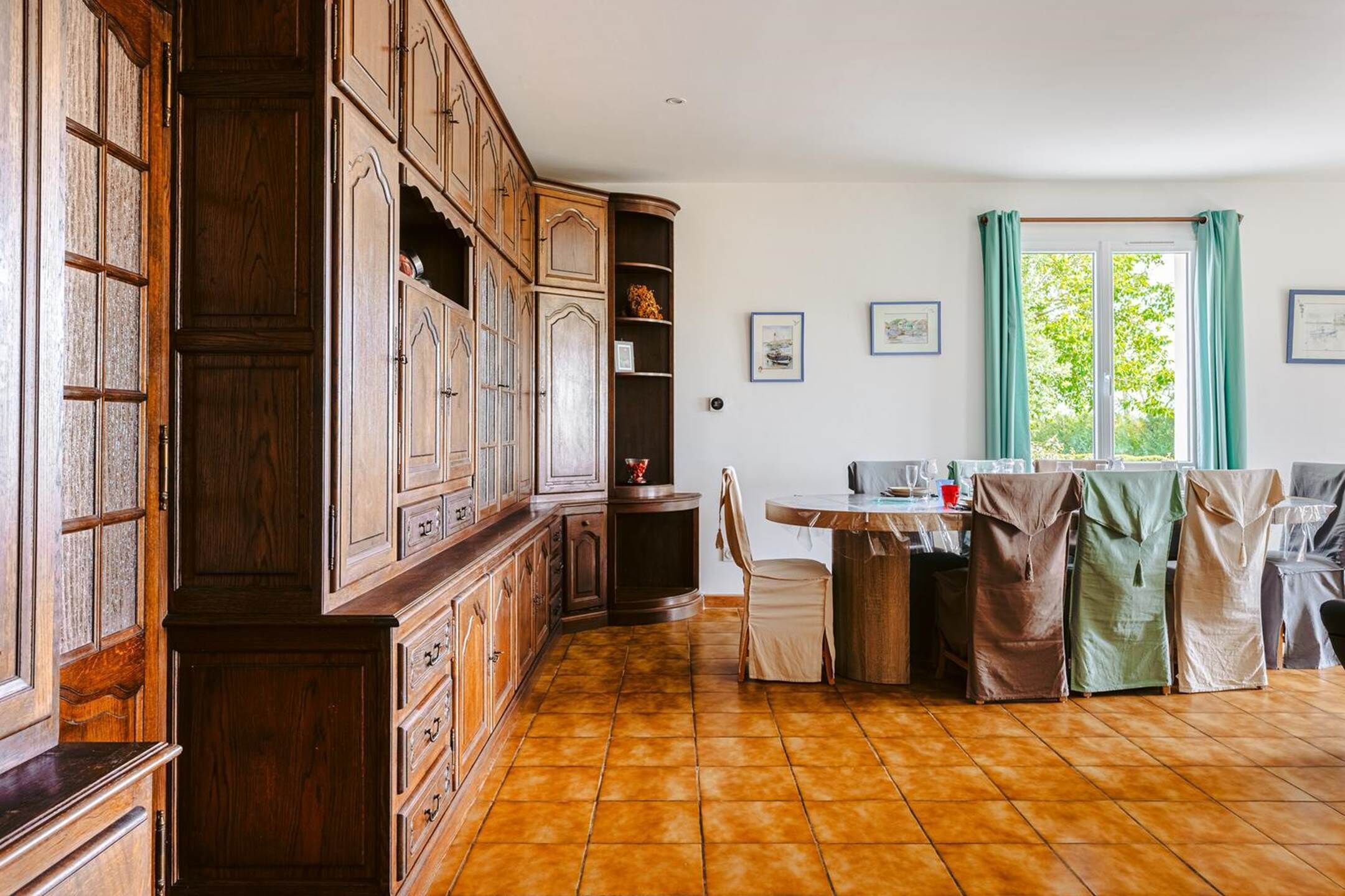 A traditional kitchen with wooden cabinets, a tiled floor, and a dining area with chairs and a table.