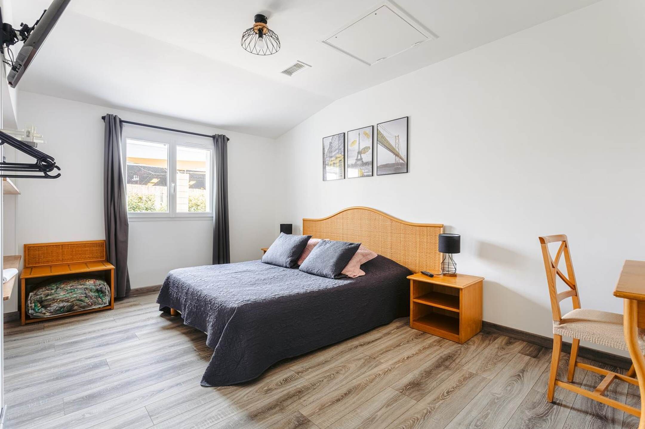 A bedroom with a bed, wooden nightstands, a chair, a desk, and a window with curtains.