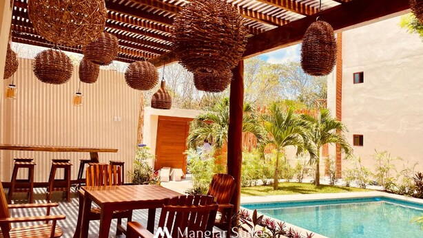 An outdoor dining area with a pool, wooden furniture, and hanging wicker lamps. - Hotel Manglar Suites (Mahahual)