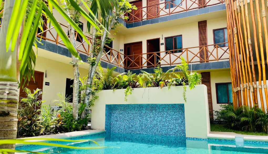Un patio de hotel con piscina, una cerca de bambú y un edificio de varios pisos con balcones.