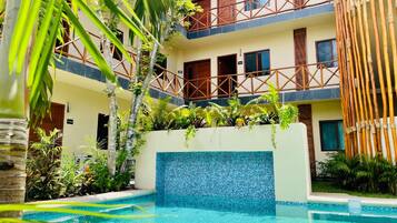 Un patio de hotel con piscina, una cerca de bambú y un edificio de varios pisos con balcones.