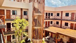 A multi-story hotel with a central atrium, wooden railings, and a staircase. - Hotel Manglar Suites (Mahahual)