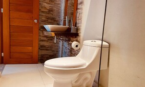 A bathroom with a white toilet, a wooden door, and a stone backsplash.