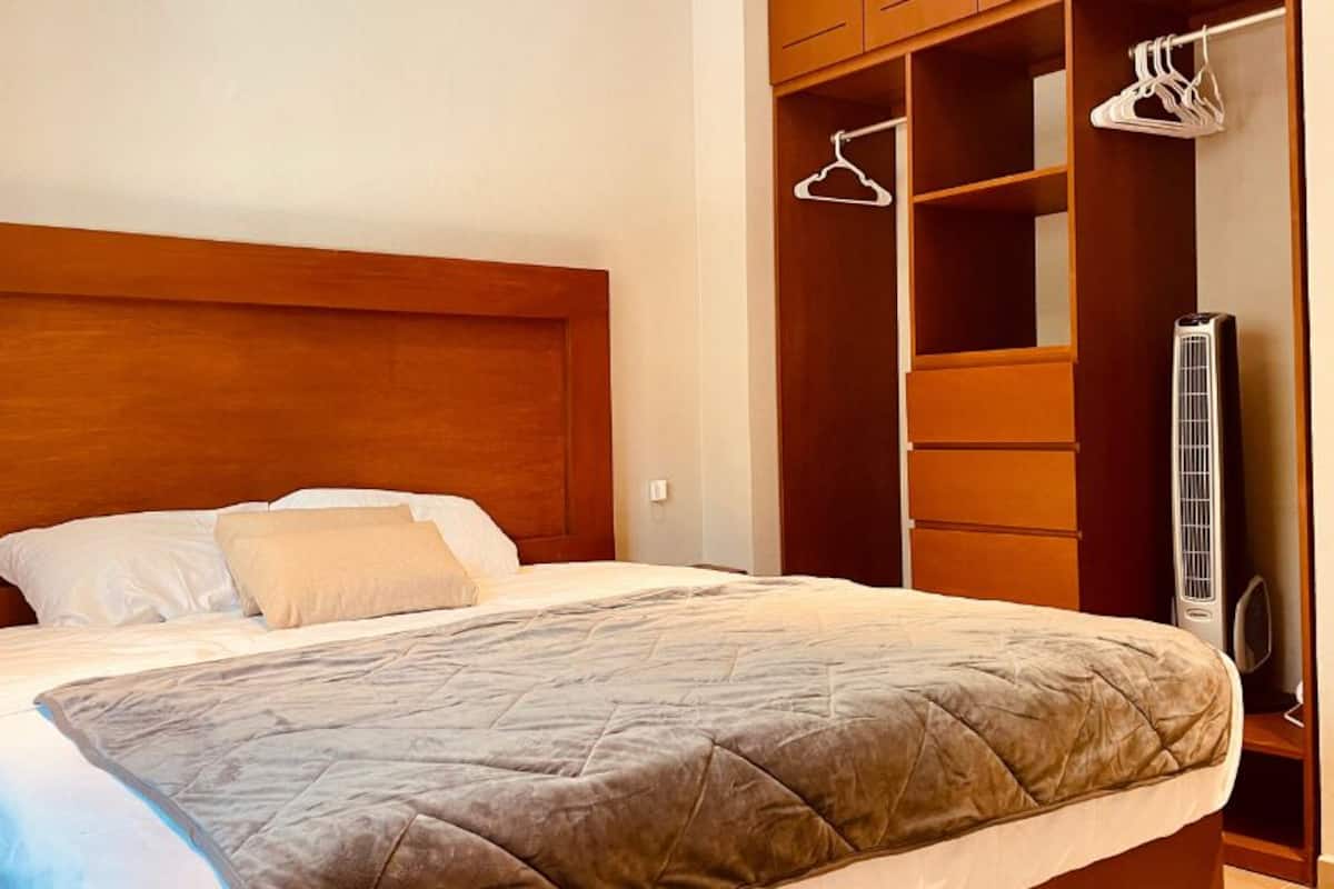 A bedroom with a large bed, wooden headboard, and a walk-in closet with hanging clothes.