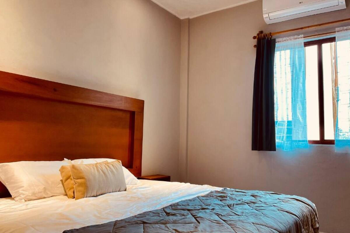 A hotel room with a wooden headboard, a bed with white bedding, and a window with blue curtains.