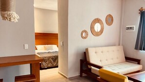 A modern hotel room with a bed, a sofa, and a small table. There are decorative wall mirrors and a hanging light fixture. - Hotel Manglar Suites (Mahahual)