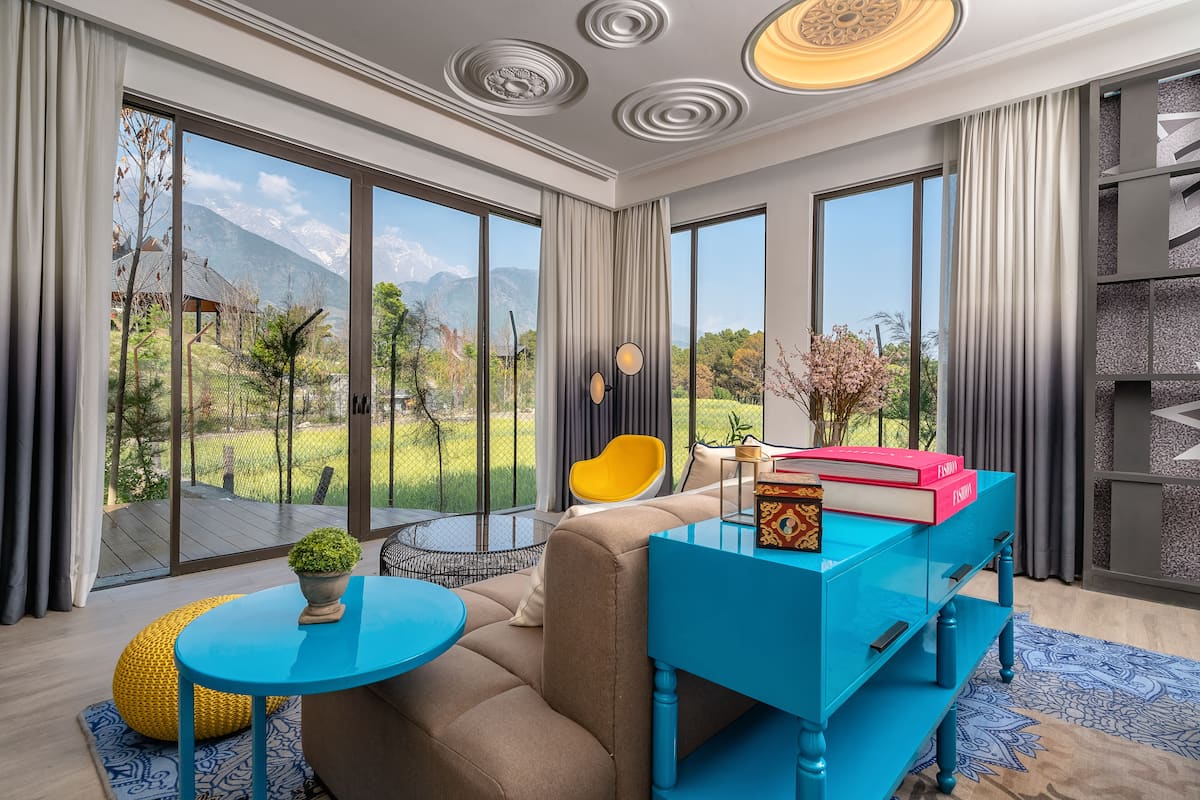 A modern living room with a sofa, a coffee table, and a blue side table. There is a view of mountains through large windows.