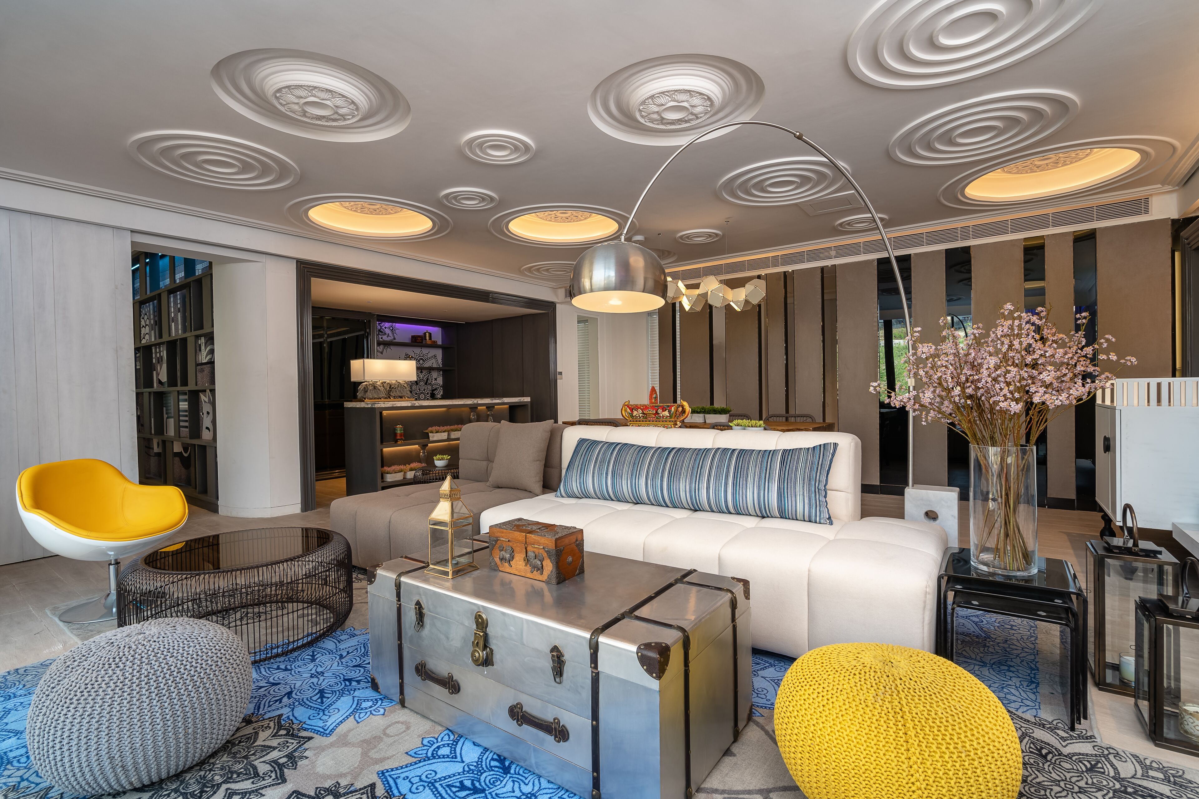 Un salon moderne avec un canapé blanc, un fauteuil jaune, une table basse en métal et un tapis à motifs.