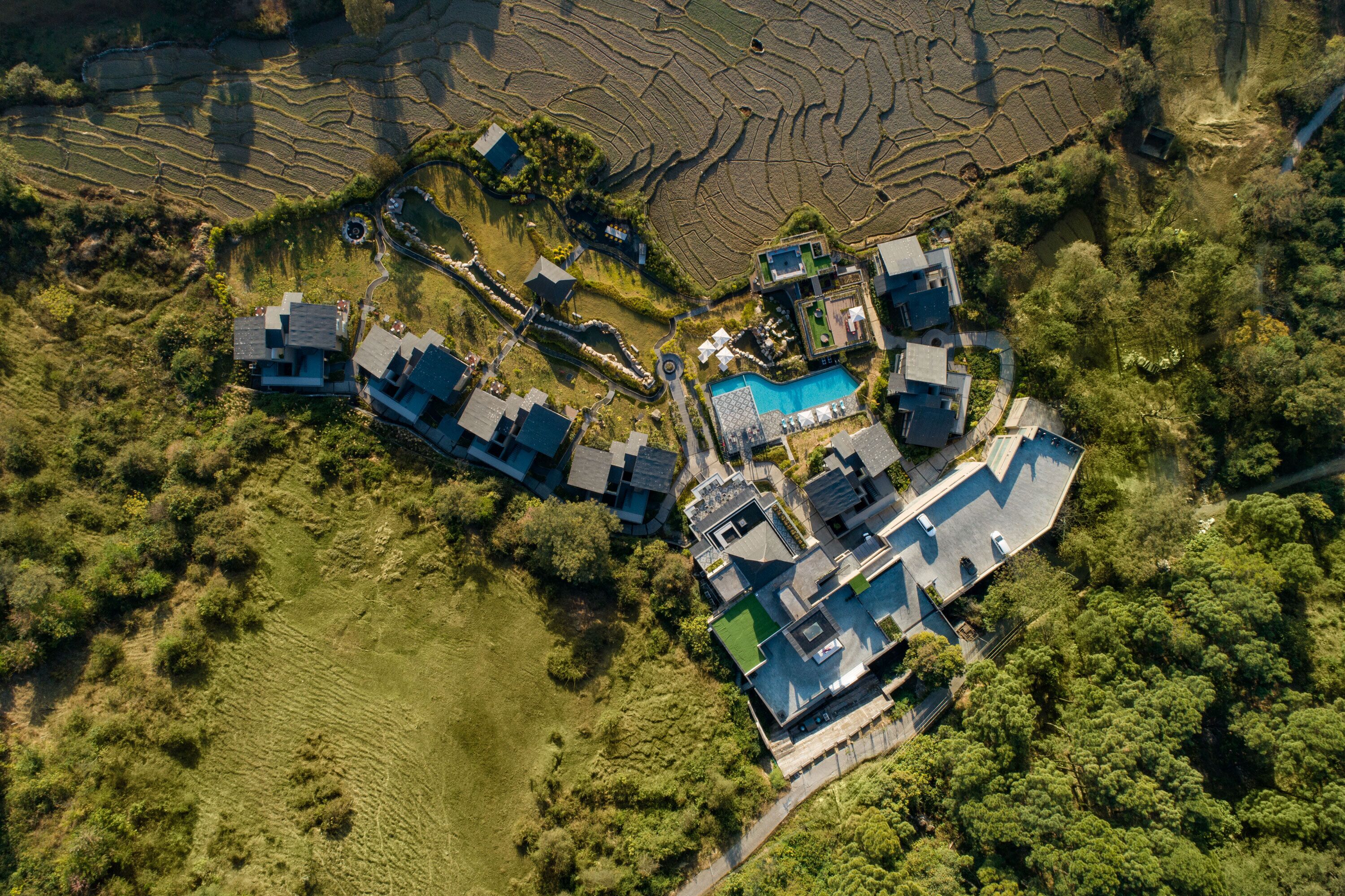 Vista aerea di una zona residenziale con diverse case, una piscina e campi a terrazze.