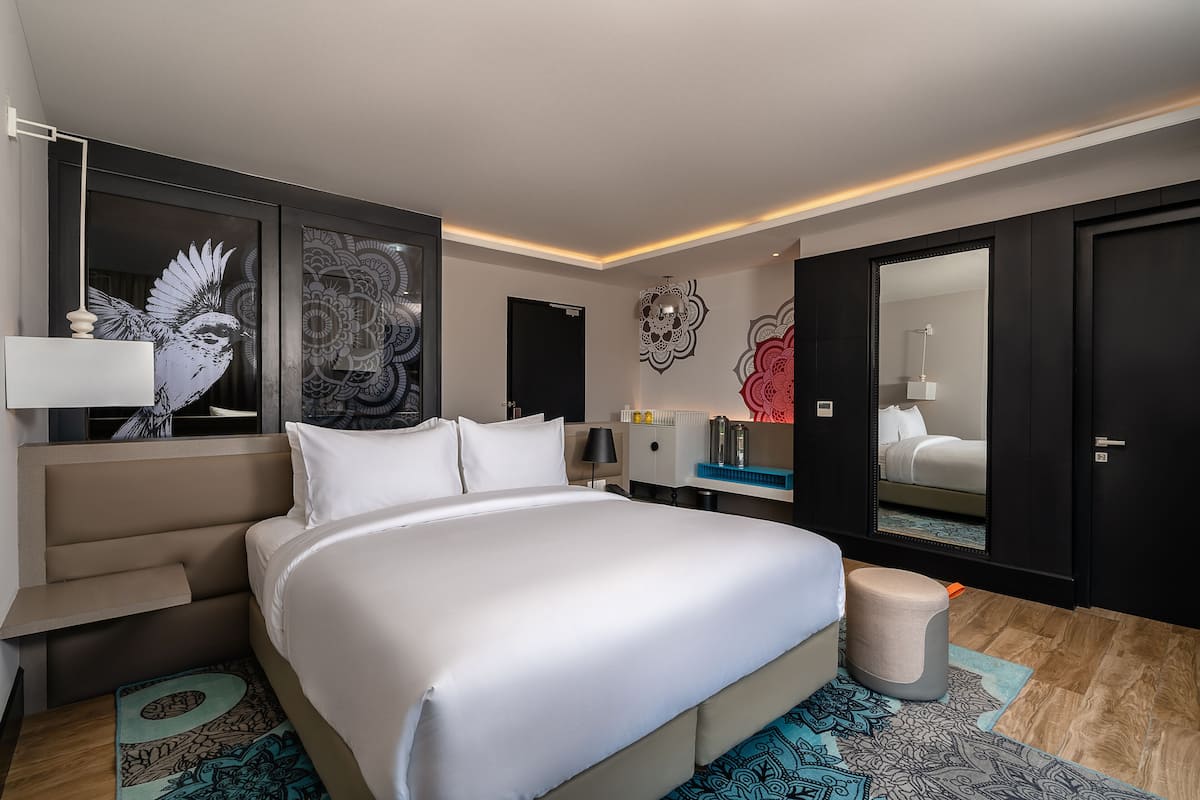A modern hotel room with a large bed, a nightstand, a mirror, and decorative wall art.