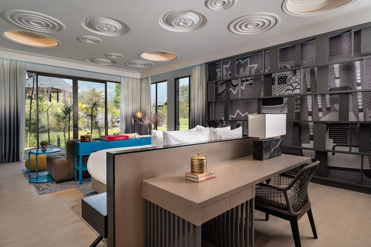 A modern hotel room with a large bed, a desk, and a view of the outdoors.