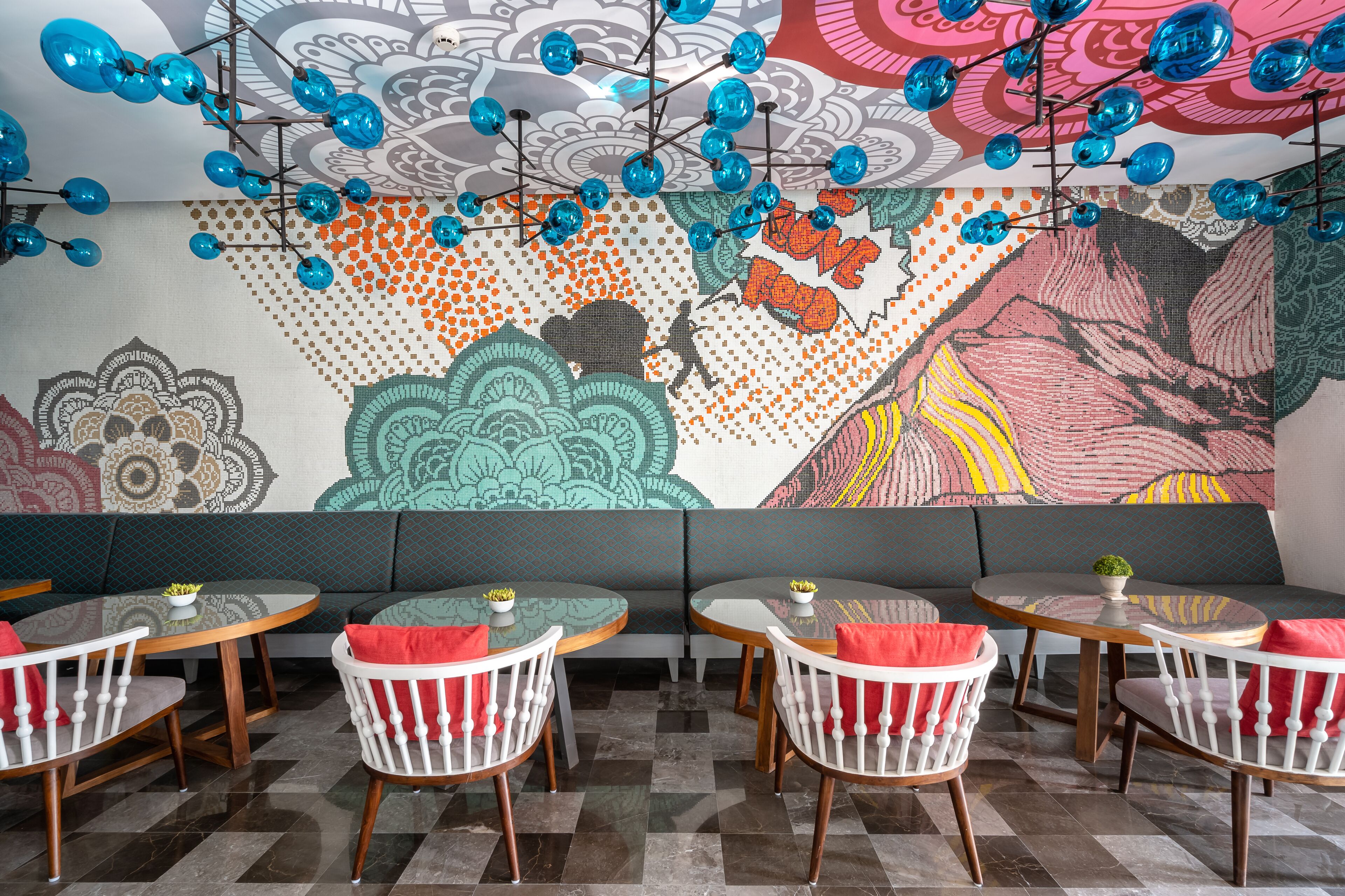 Ein Restaurantinneres mit runden Tischen, weißen Stühlen und einem farbenfrohen Wandgemälde.