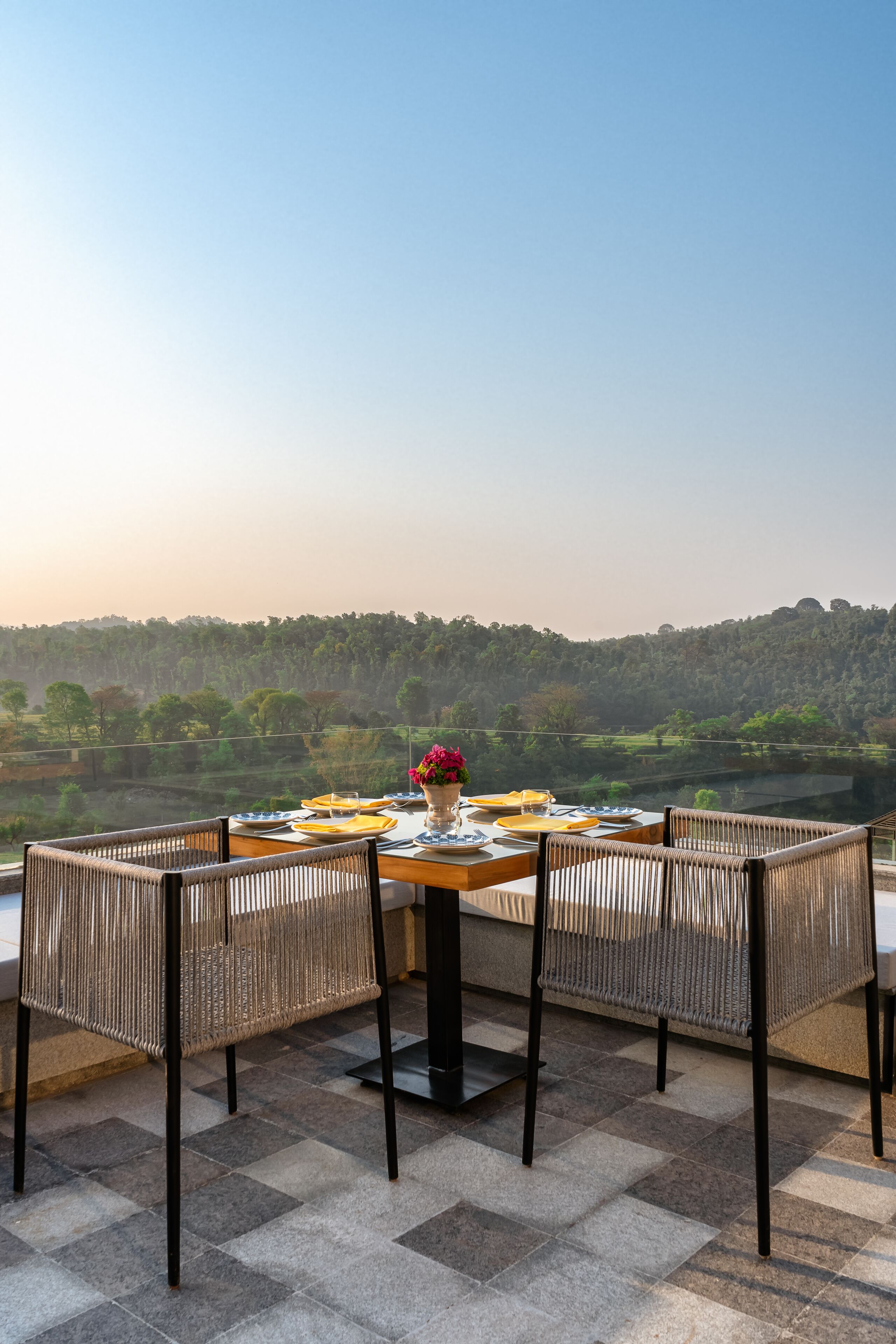 Une table dressée pour quatre personnes, entourée de chaises en osier, avec vue sur un paysage magnifique.