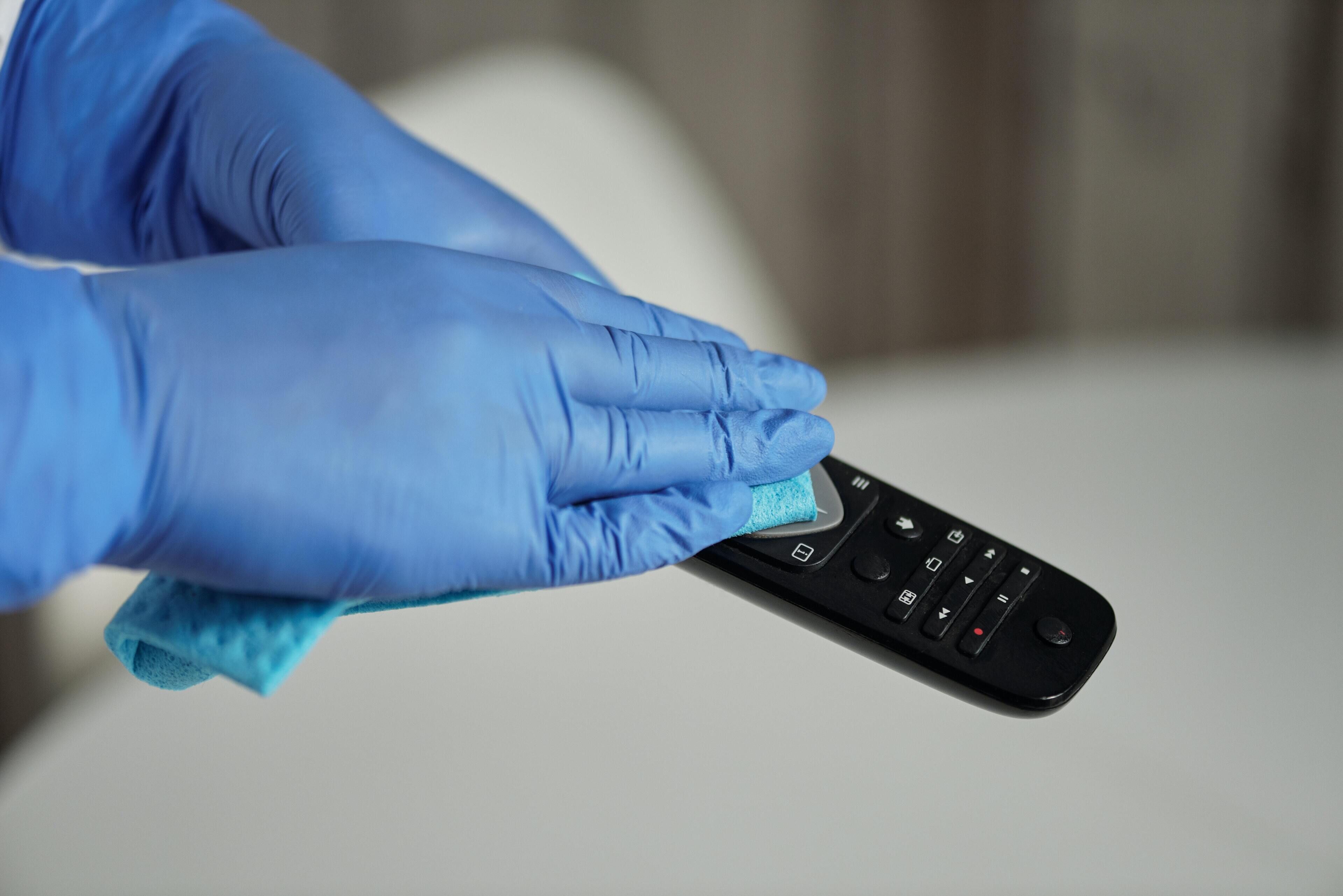 Une personne portant des gants bleus nettoie une télécommande noire avec un chiffon bleu.
