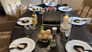 A round dining table set with plates, cutlery, a candle, a bottle, and a basket of potatoes.