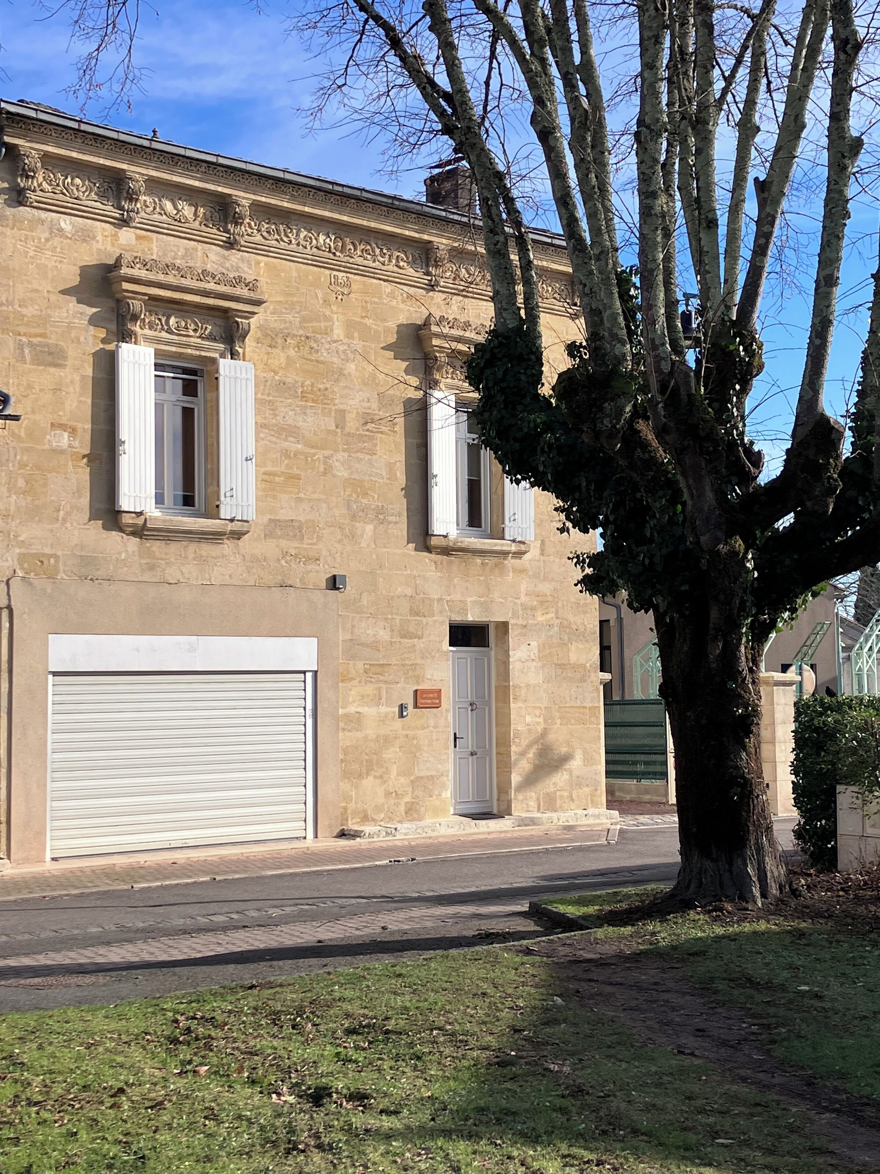 A stone building with two windows, a garage door, and a tree in front.