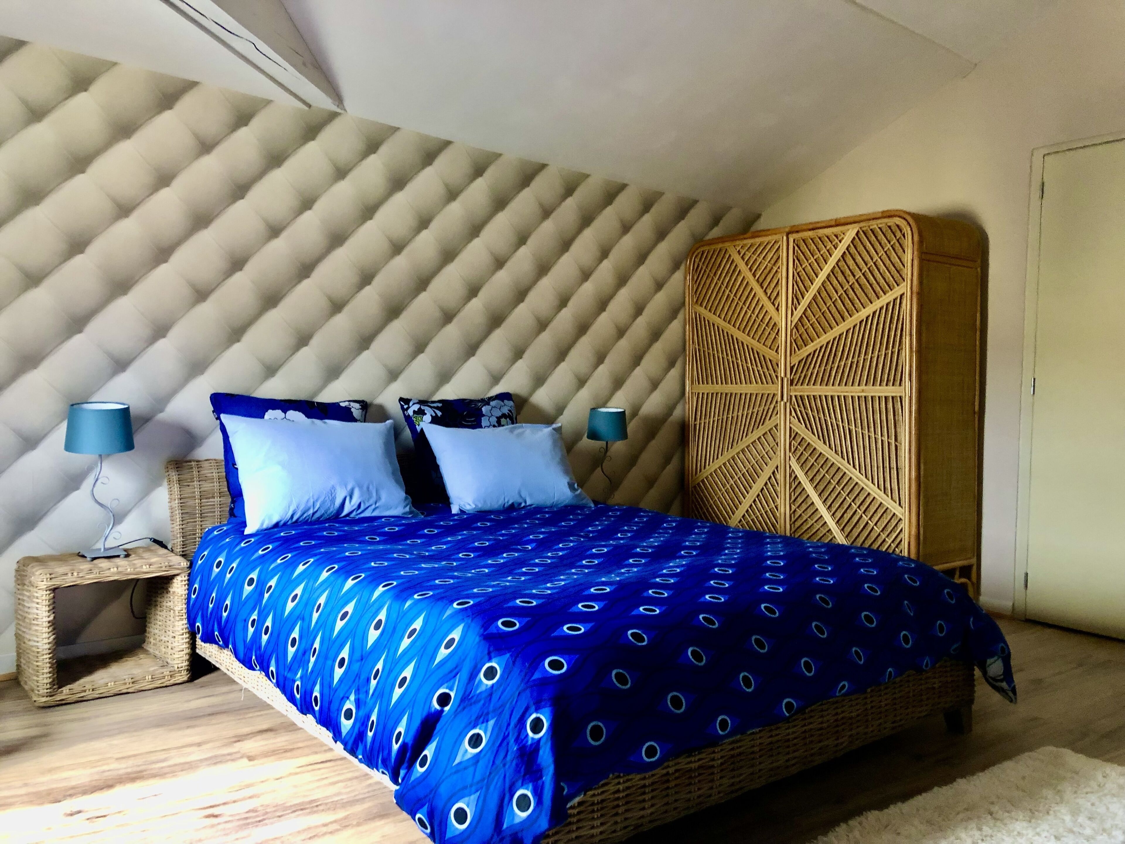 A bedroom with a bed, two bedside tables, a wall with a geometric pattern, and a wooden cabinet.