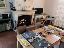 Un comedor acogedor con chimenea, televisión y una mesa lista para el desayuno, con cruasanes y fruta.