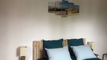 A bedroom with a wooden headboard, two pillows, a bedside table with a lamp, and a wall-mounted artwork of a beach scene.
