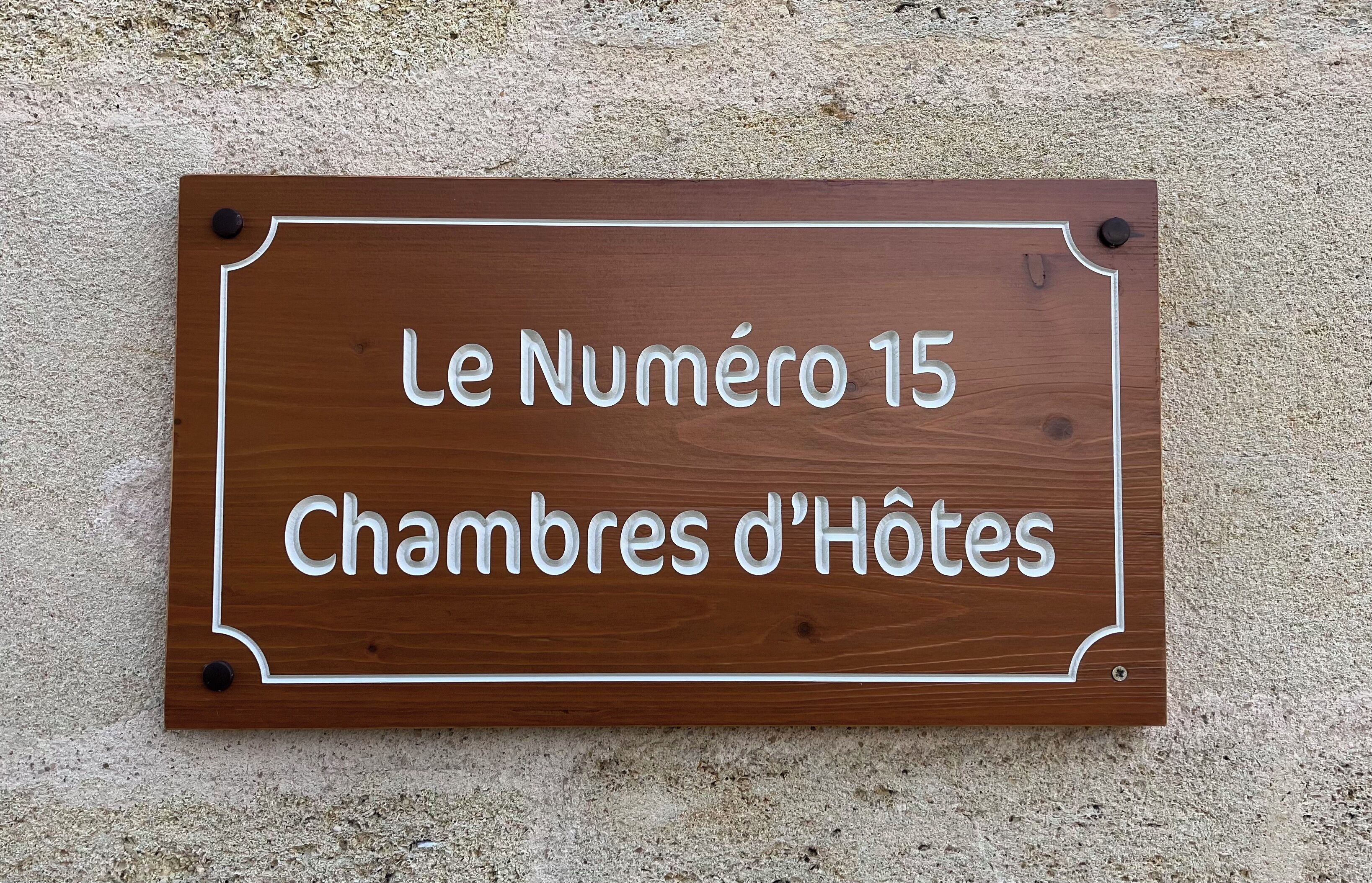 En träskylt med texten ”Le Numéro 15 Chambres d’Hôtes” som är fastsatt på en vägg med en tydlig struktur.