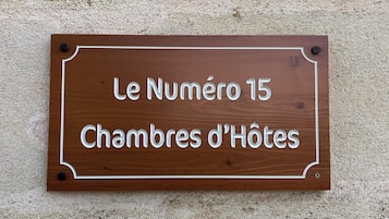 En träskylt med texten ”Le Numéro 15 Chambres d’Hôtes” som är fastsatt på en vägg med en tydlig struktur.