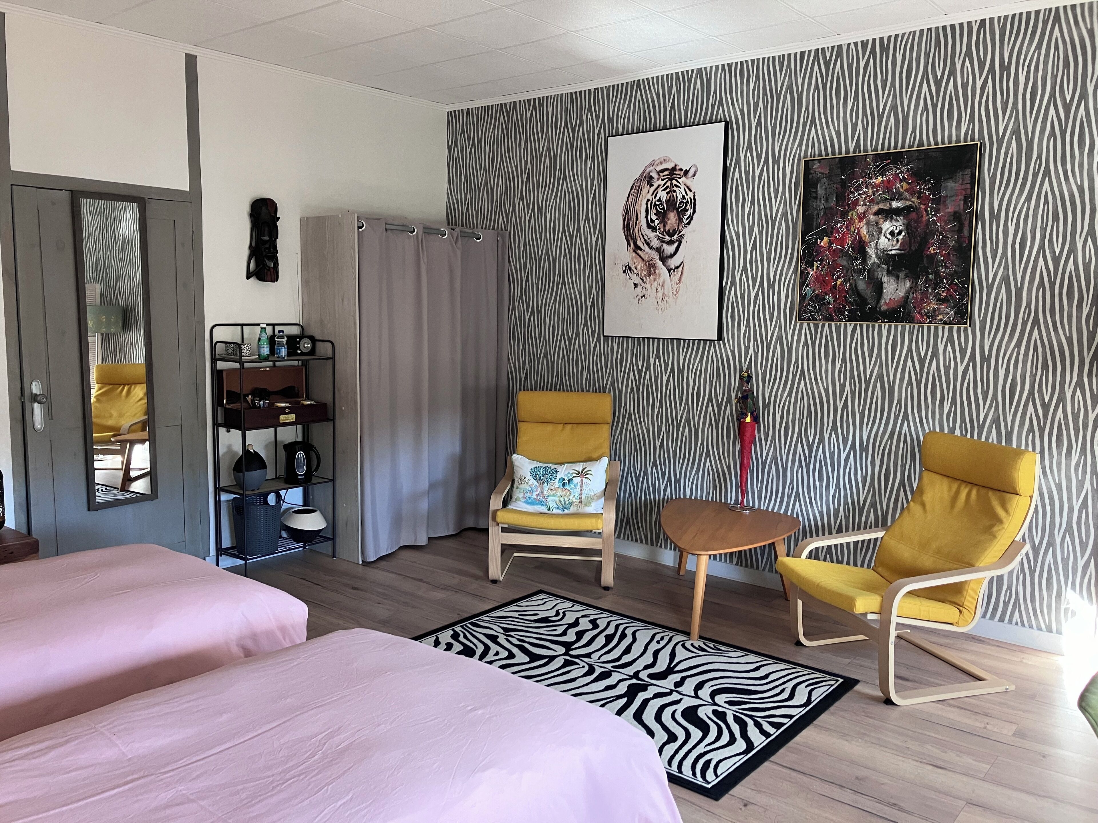 A hotel room with two beds, a zebra-patterned wall, a yellow armchair, a small table, and a mirror.