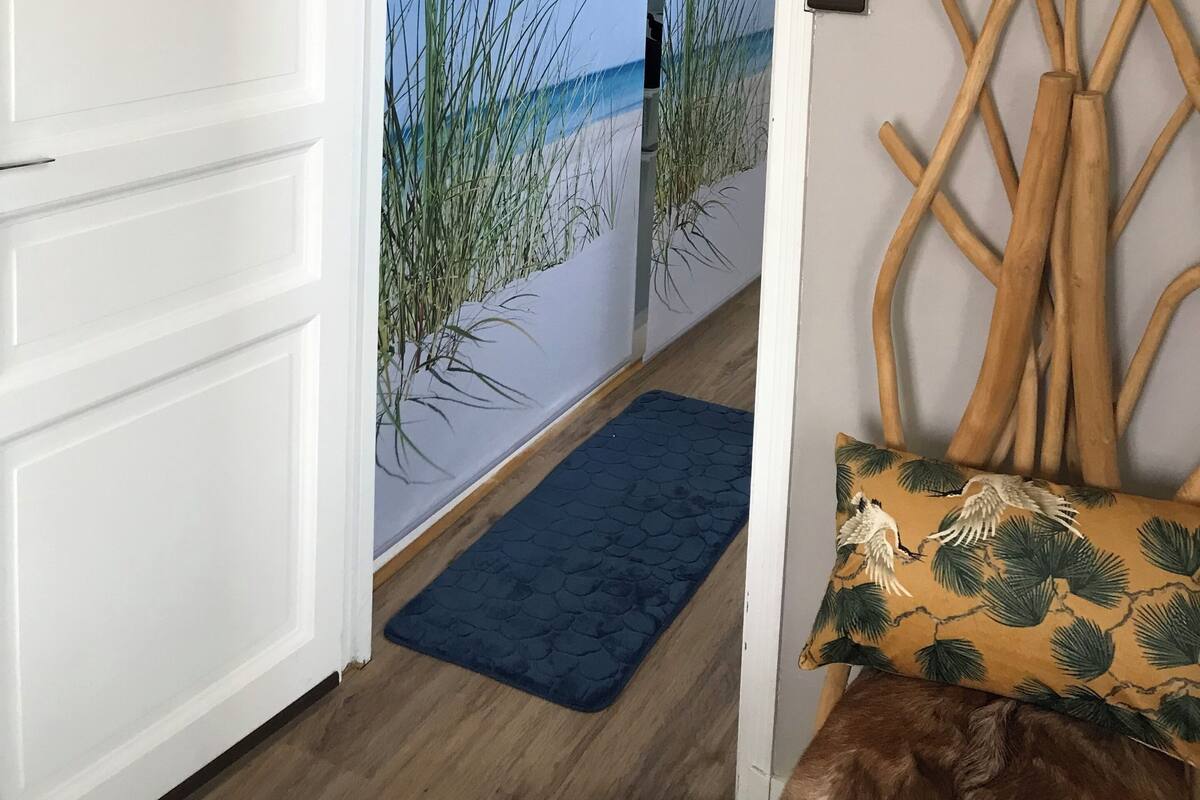 A doorway leading to a beach scene with a blue mat and a wooden sculpture.