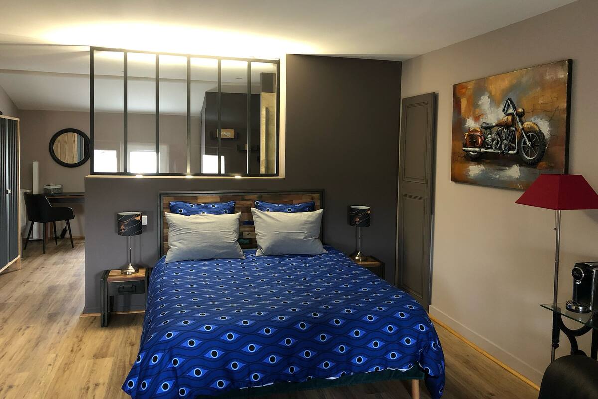 A bedroom with a bed, bedside tables, a mirror, a painting, and a desk with a chair.