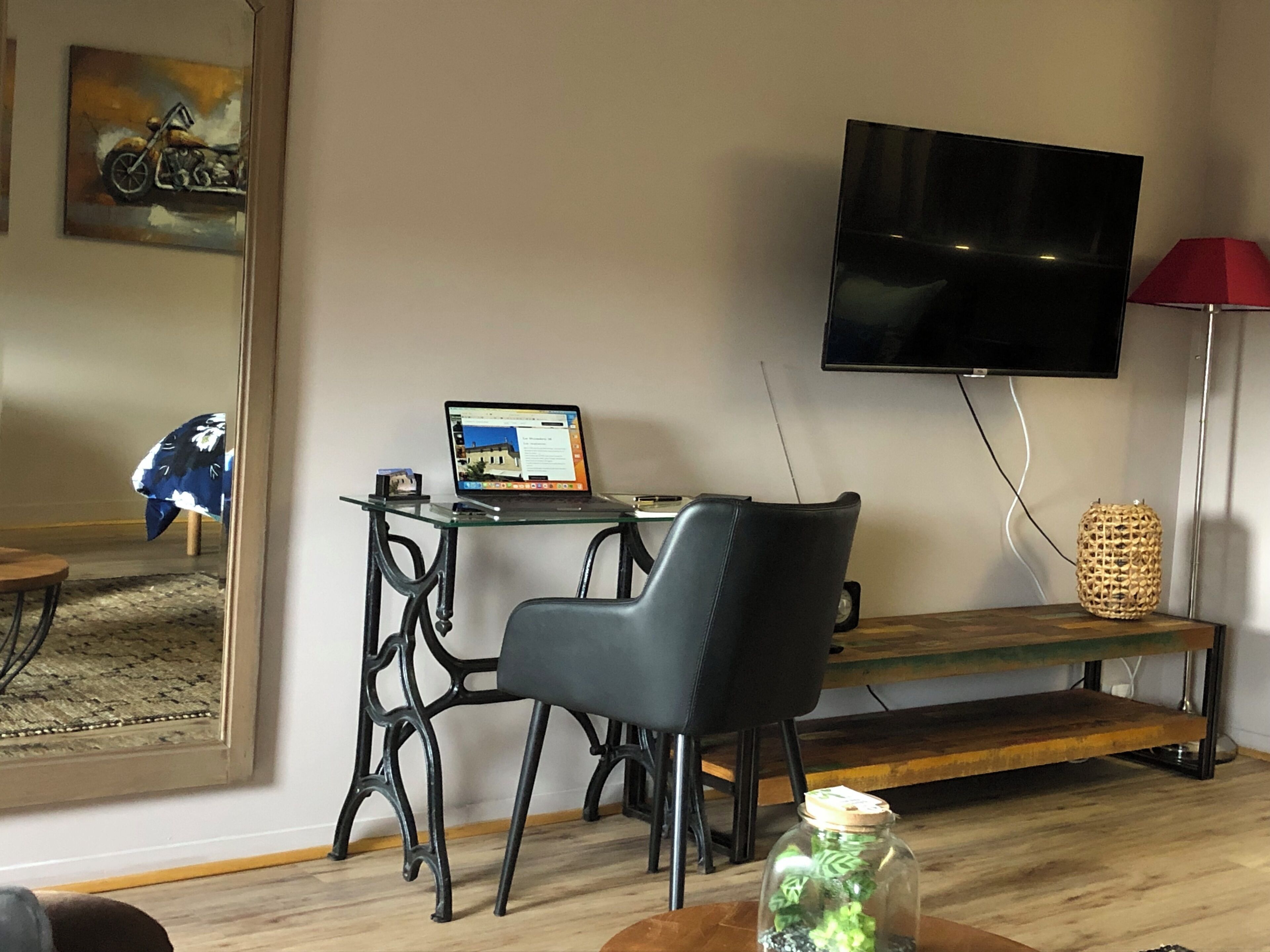 Una sala de estar moderna con una mesa de centro de vidrio, un sillón de cuero negro, un banco de madera, un televisor montado en la pared y un frasco decorativo pequeño en el suelo.