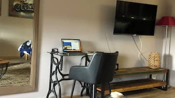 Una sala de estar moderna con una mesa de centro de vidrio, un sillón de cuero negro, un banco de madera, un televisor montado en la pared y un frasco decorativo pequeño en el suelo.