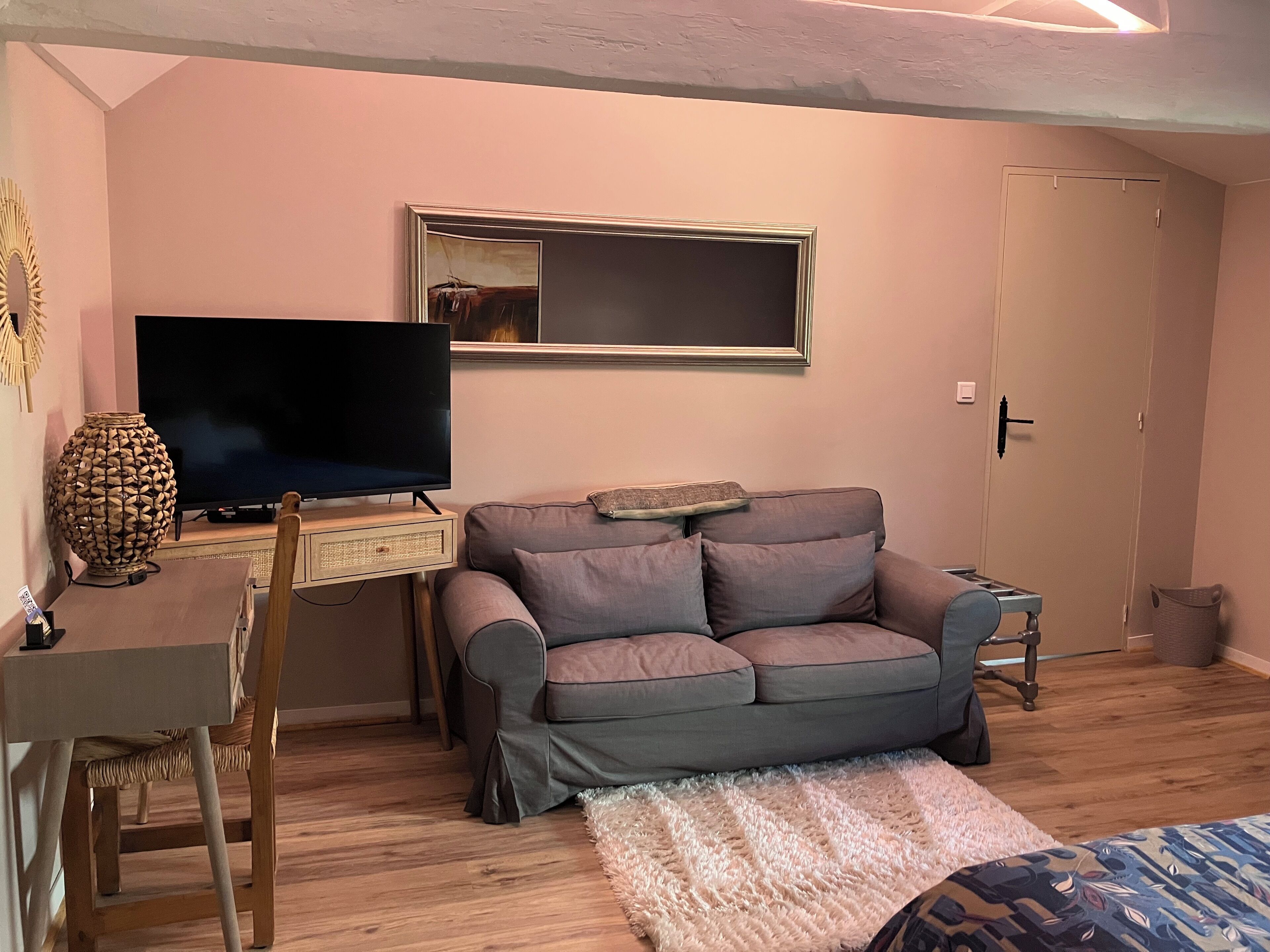 Un salon confortable avec un téléviseur, un canapé, une petite table et un vase décoratif.