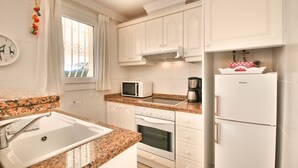 A kitchen with white cabinets, a granite countertop, a microwave, a coffee maker, an oven, and a refrigerator. - Beautiful Villa with pool in Oliva Nova Golf (Oliva)