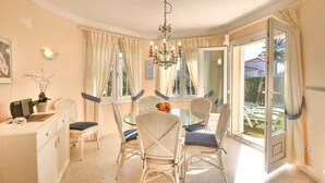 A dining area with a glass table, white wicker chairs, a chandelier, and a view of the outdoors. - Beautiful Villa with pool in Oliva Nova Golf (Oliva)