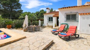Une terrasse en pierre avec une piscine, du mobilier d’extérieur et un bâtiment blanc doté d’un toit recouvert de tuiles.