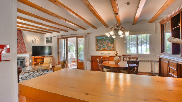 Un vaste espace de vie doté d’un plafond en bois, d’une grande table à manger en bois et d’un téléviseur placé dans un coin.