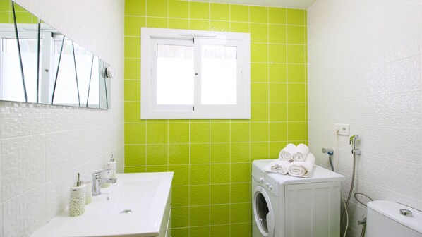 A bathroom with a white sink, a mirror, a window, a washing machine, and a toilet.