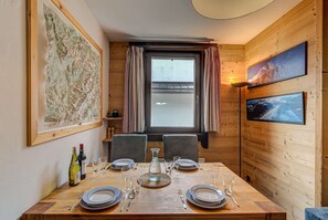 A dining area with a wooden table set for four, a large map on the wall, and a window with curtains.