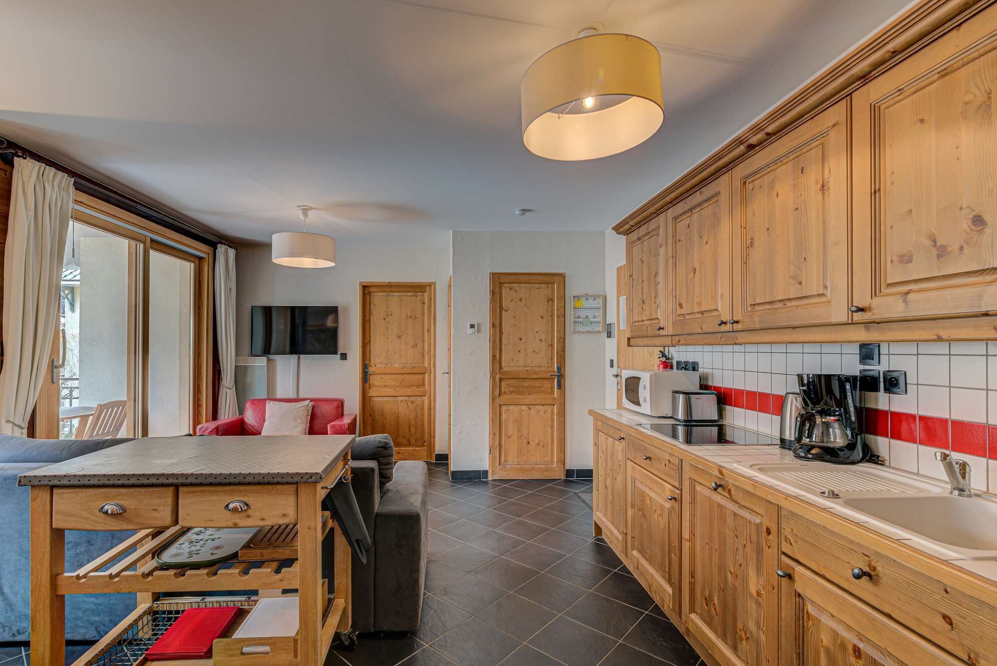 Una cocina compacta con armarios de madera, salpicadero de azulejos y una zona de comedor con una silla roja y una mesa.