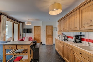 A compact kitchen with wooden cabinets, a tiled backsplash, and a dining area with a red chair and a table.